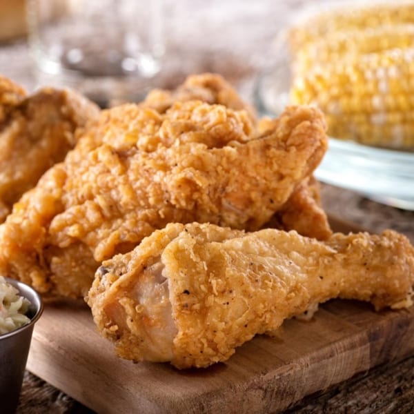 Crispy fried chicken pieces on a wooden board, with corn on the cob and coleslaw in the background.