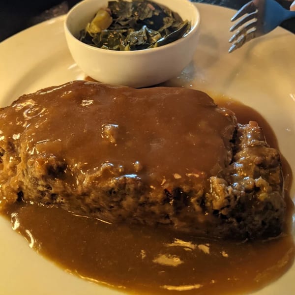 Southern meatloaf with brown gravy and a side of collard greens on a white plate.