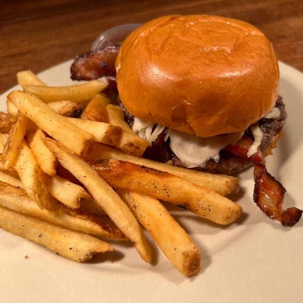 A Southern-style burger with bacon and fries on a white plate at Annie O's Kitchen.